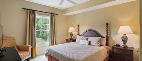 A bedroom with a bed, two nightstands, a desk, a chair, a window with curtains, and a ceiling fan.
