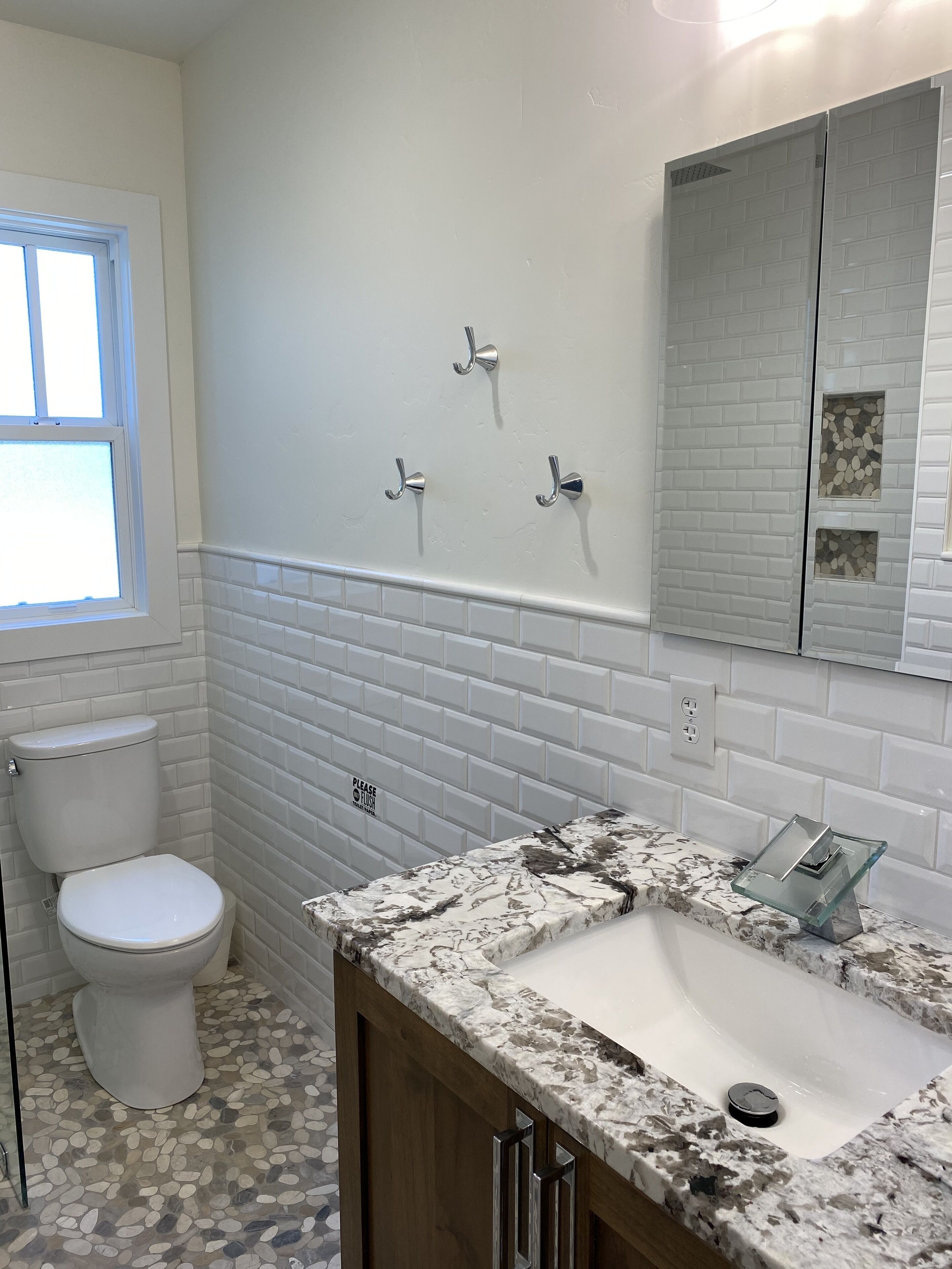 Une salle de bain avec des toilettes blanches, un lavabo doté d’un plan de travail en marbre et un miroir avec un pare-feu en forme de motifs de briques.
