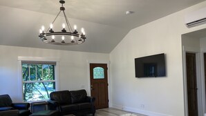 A spacious living room with a large chandelier, a flat-screen TV mounted on the wall, and a door leading to another room. - ***NEW*** Charming home located in Downtown Bend! (Bend)