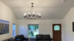 A living room with a chandelier, leather sofas, a coffee table, and a large window with a view of greenery. - ***NEW*** Charming home located in Downtown Bend! (Bend)