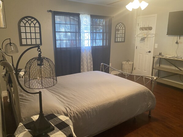 A bedroom with a large bed, a desk with a chair, a window with curtains, and a wall-mounted TV. - Newly Renovated Farmhouse! (Sebring)