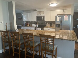 A kitchen with granite countertops, wooden chairs, white cabinets, a stainless steel refrigerator, and a microwave. - Newly Renovated Farmhouse! (Sebring)
