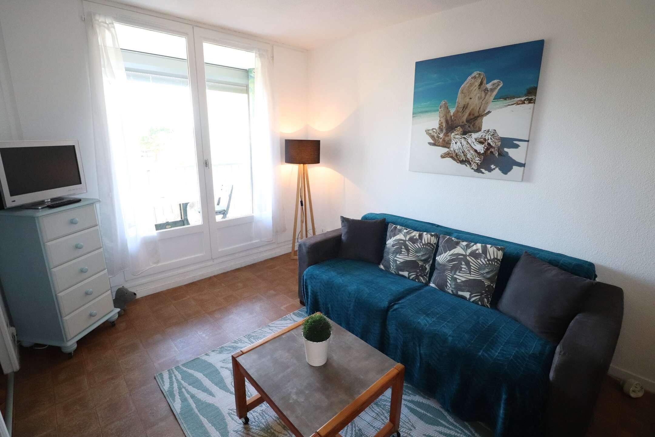 Una sala de estar con un sofá, una mesita con una planta, un televisor en un mueble y un cuadro en la pared.