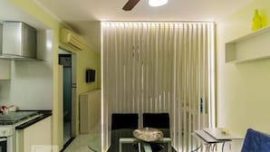 A compact kitchen with a stove, a microwave, and a ceiling fan. There is a dining area with a table and chairs, and a window with vertical blinds. - In the best place in higienopolis 1 bedroom 1vaca (SP)