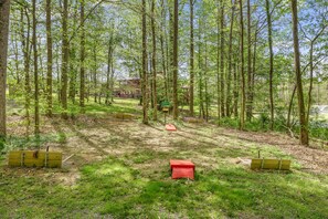 A forested area with a dirt path leading to a building. There are wooden benches and a red object in the foreground. - 2 bd Cabin, Hot tub, UTK/Neyland, Smokys, 16acres, FP, Arcade, Fishing (Knoxville)