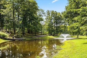 A serene park with a pond, a fountain, and a wooden deck.