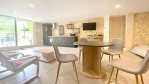 Ein modernes Wohnzimmer mit einem runden Holztisch, grau gepolsterten Sesseln, einer Couch und einem an einer Steinwand montierten Fernseher.