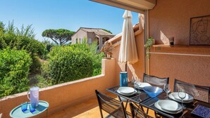 A balcony with a table set for dining, a white umbrella, and a view of a house and greenery. - Les Coteaux de la Nartelle by Interhome (Sainte Maxime)
