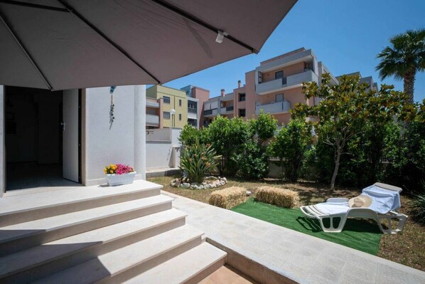 A modern outdoor area with steps leading to a covered entrance, a lounge chair, and a small garden with plants and a flower pot.