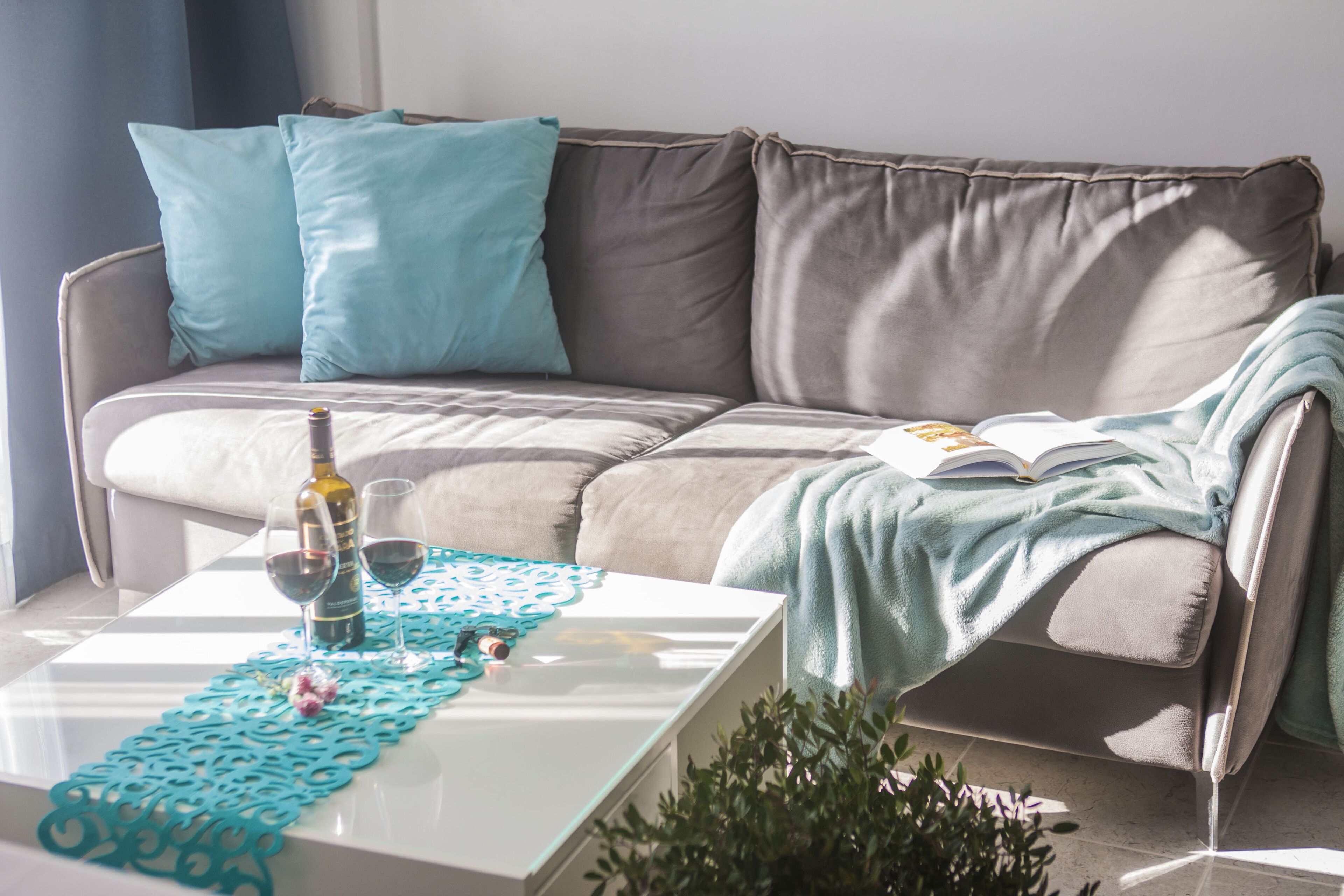 Een moderne woonkamer met een grijze bank, kussens in teal-tint, een witte salontafel en een boek.