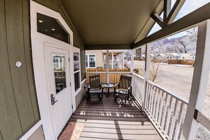 A covered porch with a wooden floor, a white door, and a view of a residential area. - Moab Tiny Home Near Arches | Sleeps 6 | Private Porch | Sand Flats (Moab)