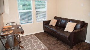A living room with a brown leather sofa, two windows with blinds, a dining table with chairs, and a patterned rug. - Moab Tiny Home Near Arches | Sleeps 6 | Private Porch | Sand Flats (Moab)