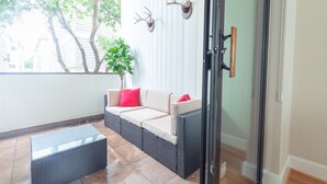 Een overdekt terras met een rieten bank, een tafel met glazen blad en decoratieve geweihangers.