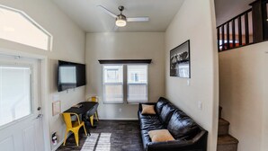 A compact living space with a black leather couch, a dining table with yellow chairs, a ceiling fan, and a staircase.