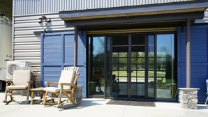 Een gebouw met een grote glazen schuindeur, terras met stoelen en een tafel, en een stenen plantenbak.