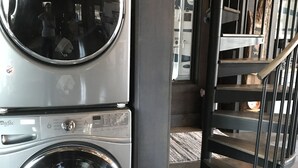 Een gestapelde wasmachine en droger in een commerciële ruimte, met een metalen trap en een betonnen vloer.