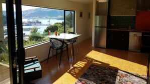 A modern kitchen with a stainless steel refrigerator, a dishwasher, and a large window overlooking a scenic view of a body of water and mountains. - Harbour Escape - tiny home in Lyttelton with Port Views (Lyttelton)