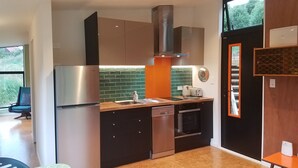 A modern kitchen with stainless steel appliances, a dishwasher, and a built-in oven. There is a window providing natural light and a view of greenery outside. - Harbour Escape - tiny home in Lyttelton with Port Views (Lyttelton)