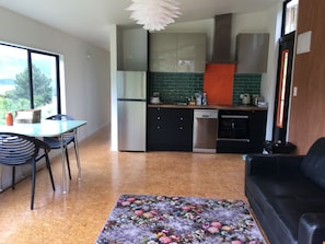 A compact living space with a dining area, kitchenette, and a sofa. - Harbour Escape - tiny home in Lyttelton with Port Views (Lyttelton)