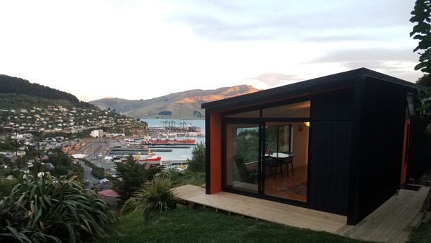 A modern house with a glass door leading to a patio with a table and chairs. - Harbour Escape - tiny home in Lyttelton with Port Views (Lyttelton)