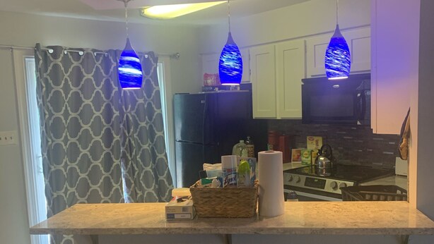 Une cuisine moderne dotée d’un îlot central, de tabourets de bar et de luminaires suspendus bleus.