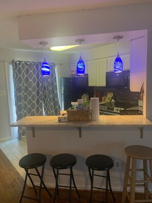 Een moderne keuken met een centraal eiland, barstoelen en blauwe hanglampen.