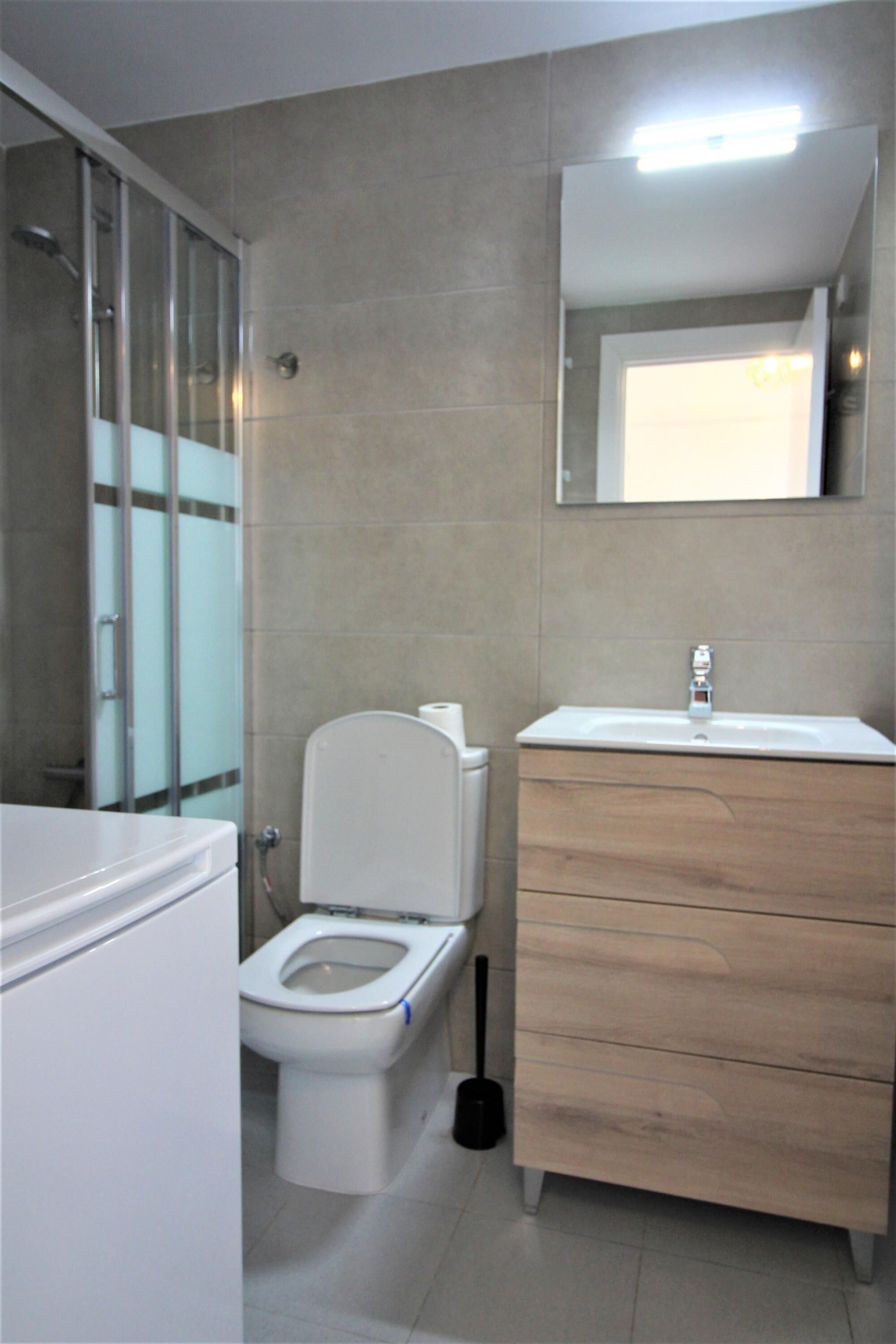 Ein Badezimmer mit Toilette, Waschbecken, Spiegel und Duschbereich.