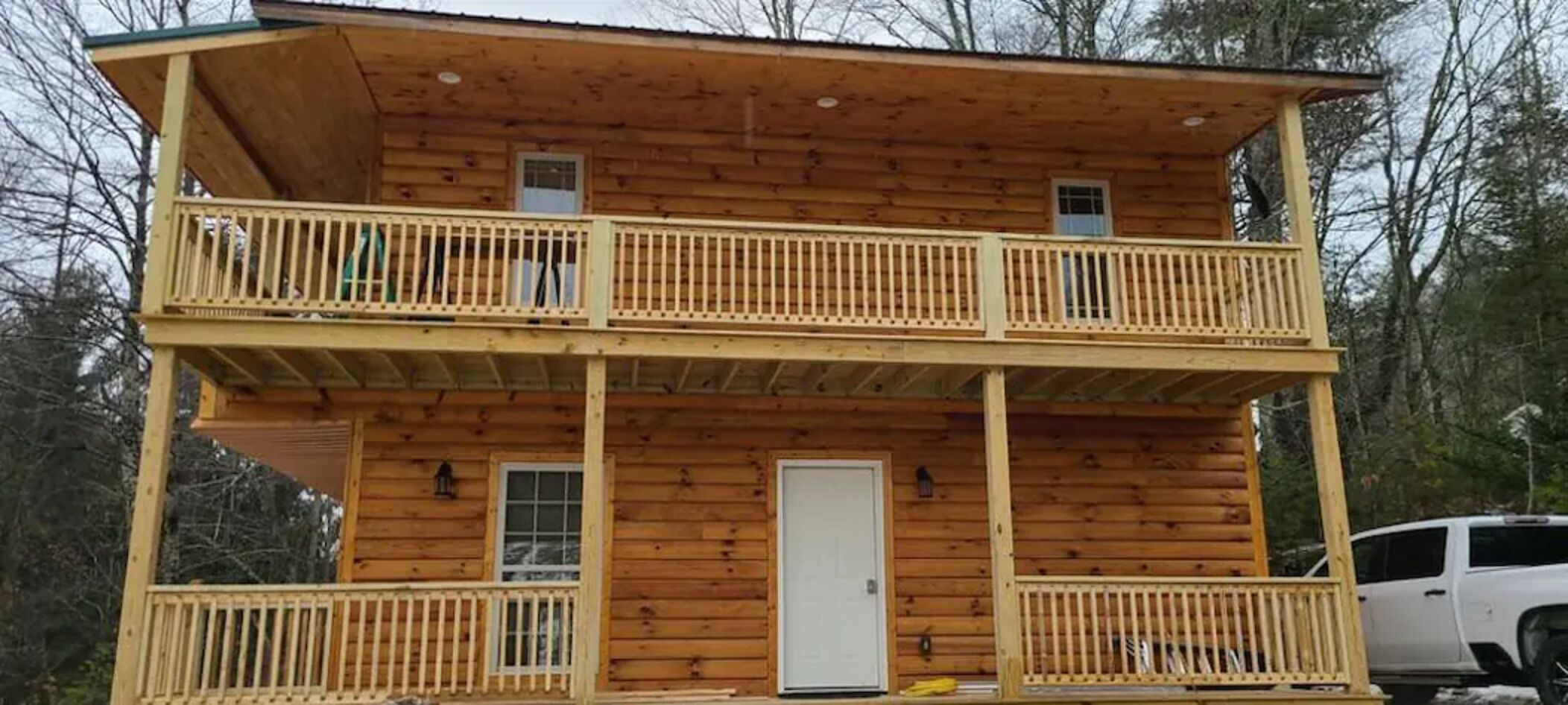 Een houten vakantiehuis met twee verdiepingen, met een balkon op elke verdieping, een voordeur en een klein raam op de bovenverdieping.