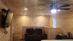A wooden cabin room with a ceiling fan, a wall-mounted TV, and a window. - Cedar Lodge, serene all wood escape in Blue Ridge (Newland)