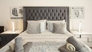 Una cama bien hecha con un cabecero capitonado, varios almohadones y dos lámparas de noche.