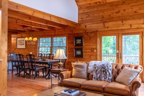 A wooden cabin interior with a dining area, leather sofa, and large windows. - Mountaintop at Yonahlossee Saddle Club - three suites, private lot, gated, views (Boone)