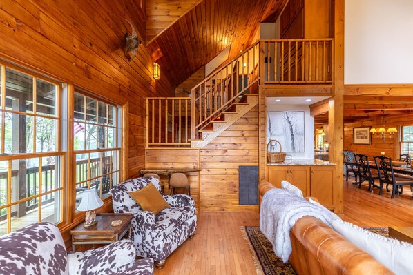 A log cabin interior with a wooden staircase, a sofa with a cowhide pattern, and a dining area with wooden furniture. - Mountaintop at Yonahlossee Saddle Club - three suites, private lot, gated, views (Boone)