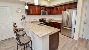 A modern kitchen with wooden cabinets, stainless steel appliances, a granite countertop, and a bar stool.