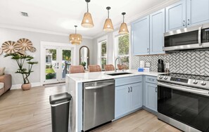 A modern kitchen with light blue cabinets, stainless steel appliances, and wicker pendant lights.