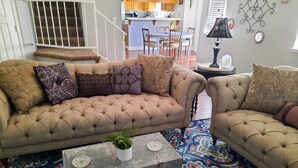 A living room with a beige tufted sofa, a coffee table, and patterned carpet. - Huge Peaceful & Cheerful Home (Redding)