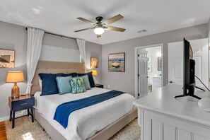 Ein Schlafzimmer mit einem Bett, einem Deckenventilator, einem Nachttisch mit Lampe, einem Schminktisch und einem Fernseher.