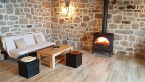 A cozy room with a stone wall, a sofa, a coffee table, and a wood-burning stove.