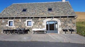 A stone building with a large arched doorway, two windows, and a patio with outdoor seating.