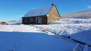 A stone building with a snow-covered roof, situated on a snowy hillside.