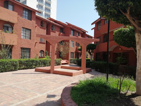 Stroll through the serene courtyard, surrounded by lush greenery and a traditional stone bench beneath a charming pergola.