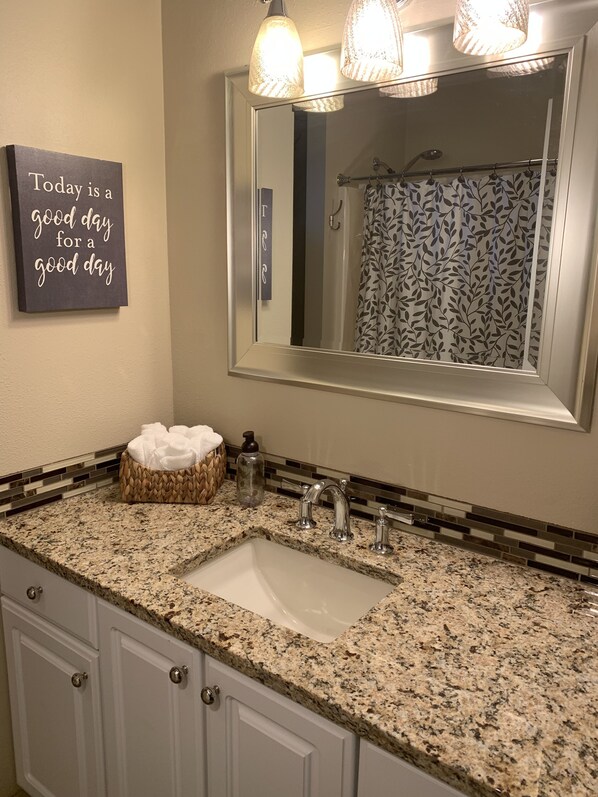 A bathroom with a granite countertop, a large mirror, a towel rack, and a motivational quote on the wall.