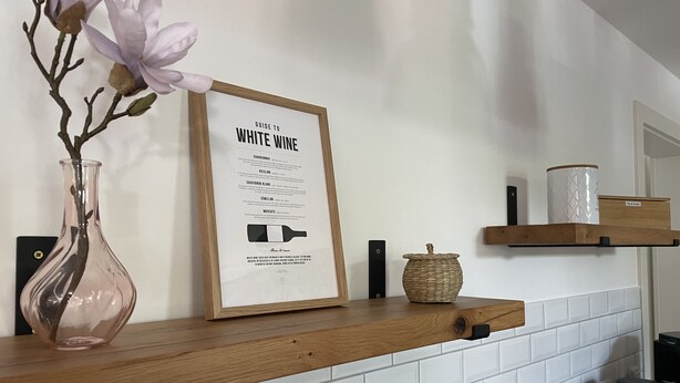 En køkkenbordplade med en ramme rundt om en guide til hvidvin, en vase med blomster og en kaffemaskine.