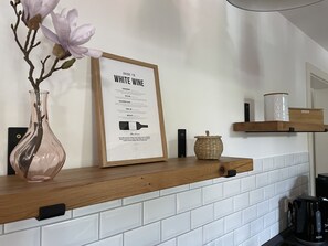 A framed guide to white wine on a kitchen counter, a vase with flowers, and a coffee maker.