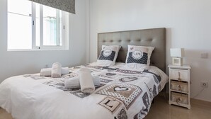 Un lit bien fait, recouvert d’une couvre-lit à motifs, avec deux oreillers décorés de motifs en forme de cœur et des serviettes enroulées posées sur le lit.