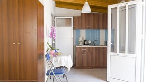 Habitación compacta con cama, una mesa de comedor con sillas, una pequeña cocina con armarios y un lavabo, y una puerta que da a otra habitación.