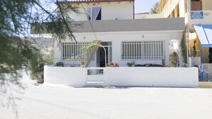 Un edificio de dos pisos con fachada blanca, un balcón y una entrada protegida por una reja.