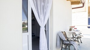 Un área de estar al aire libre techada, con una mesa, sillas, una cortina blanca y vista al interior.