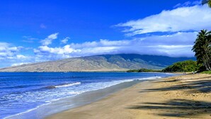 Platja amb una muntanya al fons, cel blau i aigües tranquil·les.