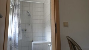 Un bany amb parets de rajola blanca, una dutxa amb plat de roba i un vàter.