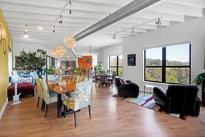 A spacious living area with a dining table, chairs, and a large window offering a view of the outdoors.
